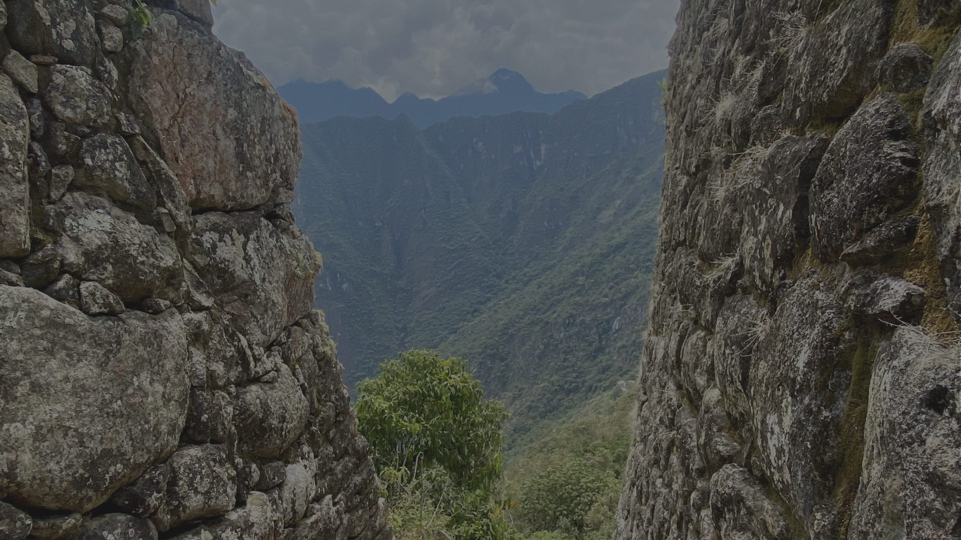 A gap between two weathered stone walls opens onto a view of mist-covered green mountains.