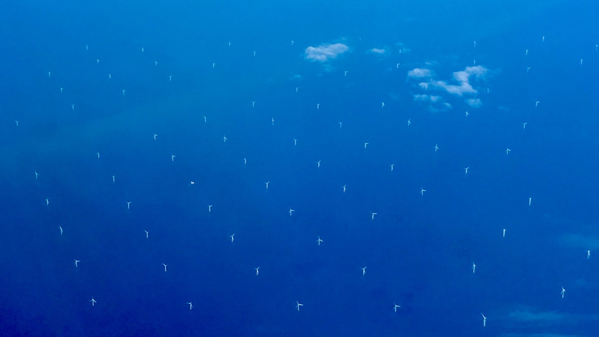 Wind turbines are scattered across open water under a partly clouded sky.