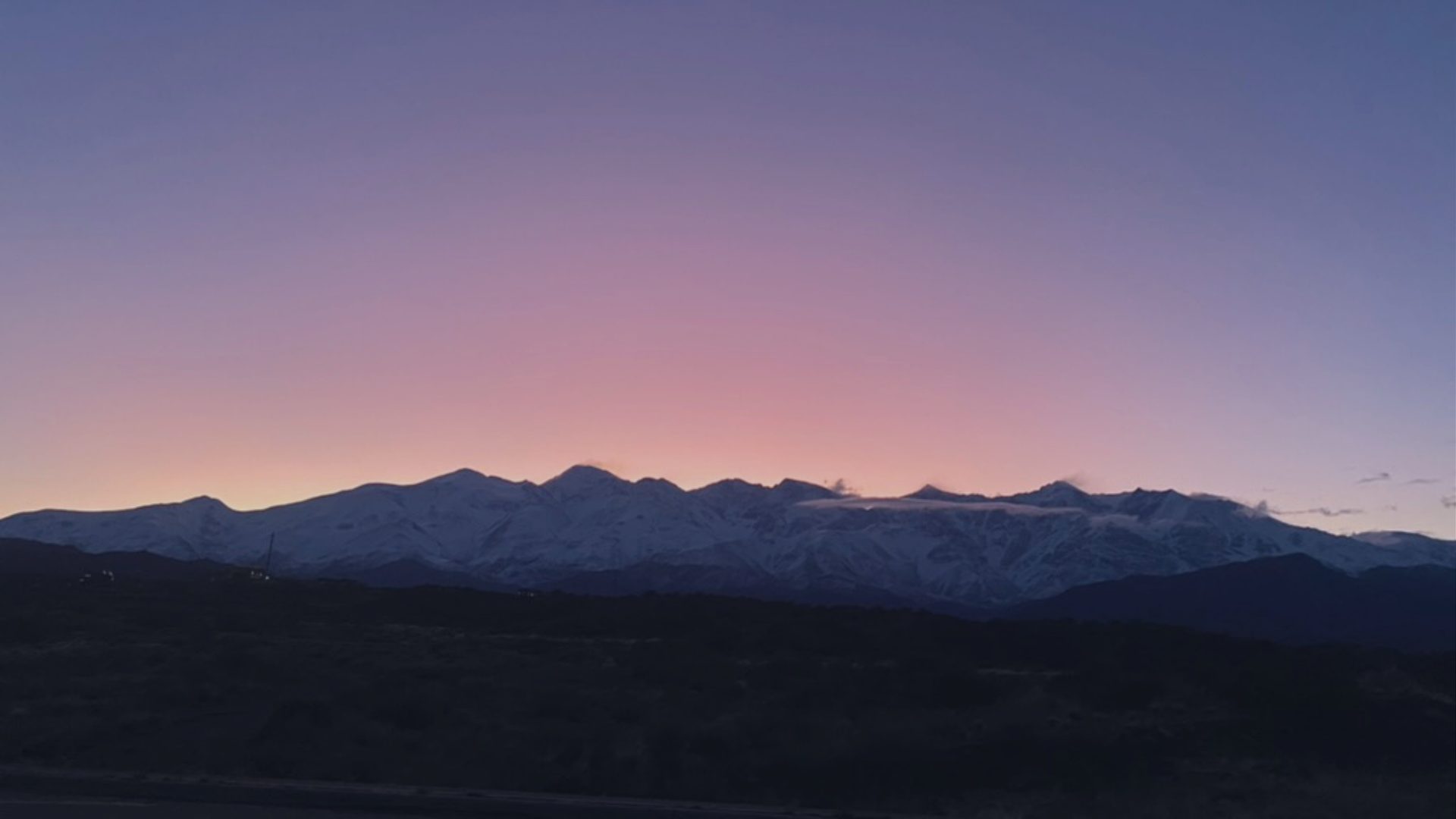 A jagged, snow-covered mountain ridge sits in silhouette under a sky fading from pink to deep blue at dusk.