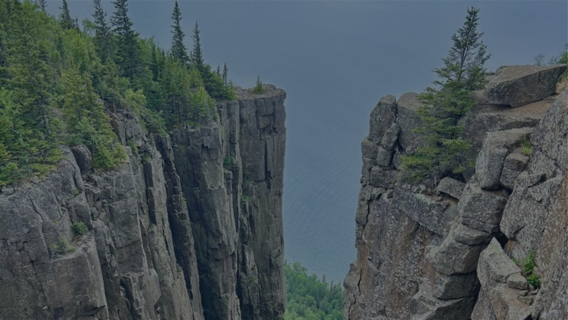 A narrow rock gorge lined with evergreen trees opens onto still water.