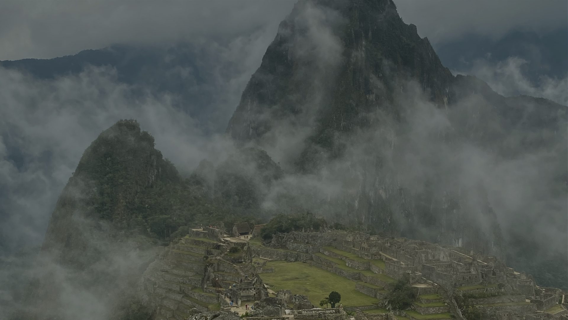 Stone ruins on a mountain ridge emerge from thick, drifting cloud.