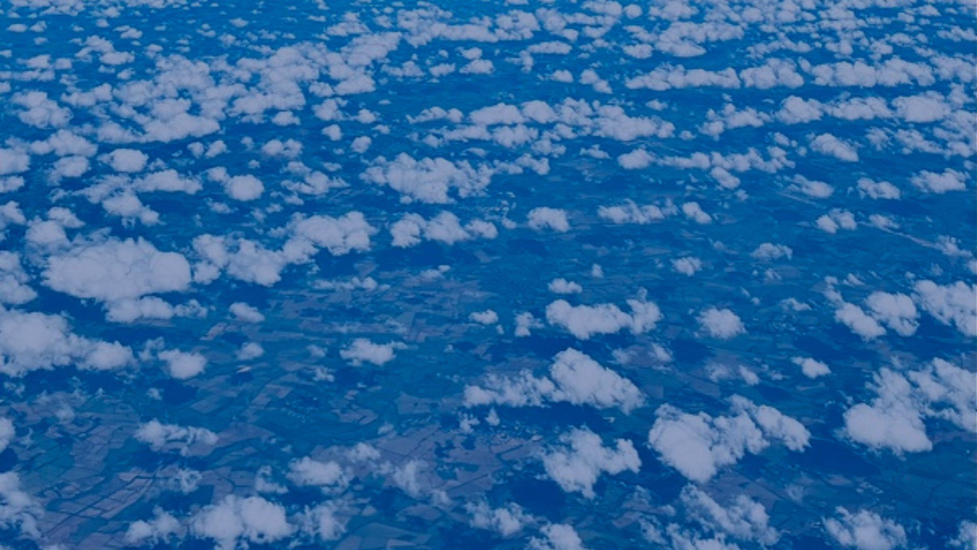 Small white clouds scatter across a deep blue sky, seen from above.