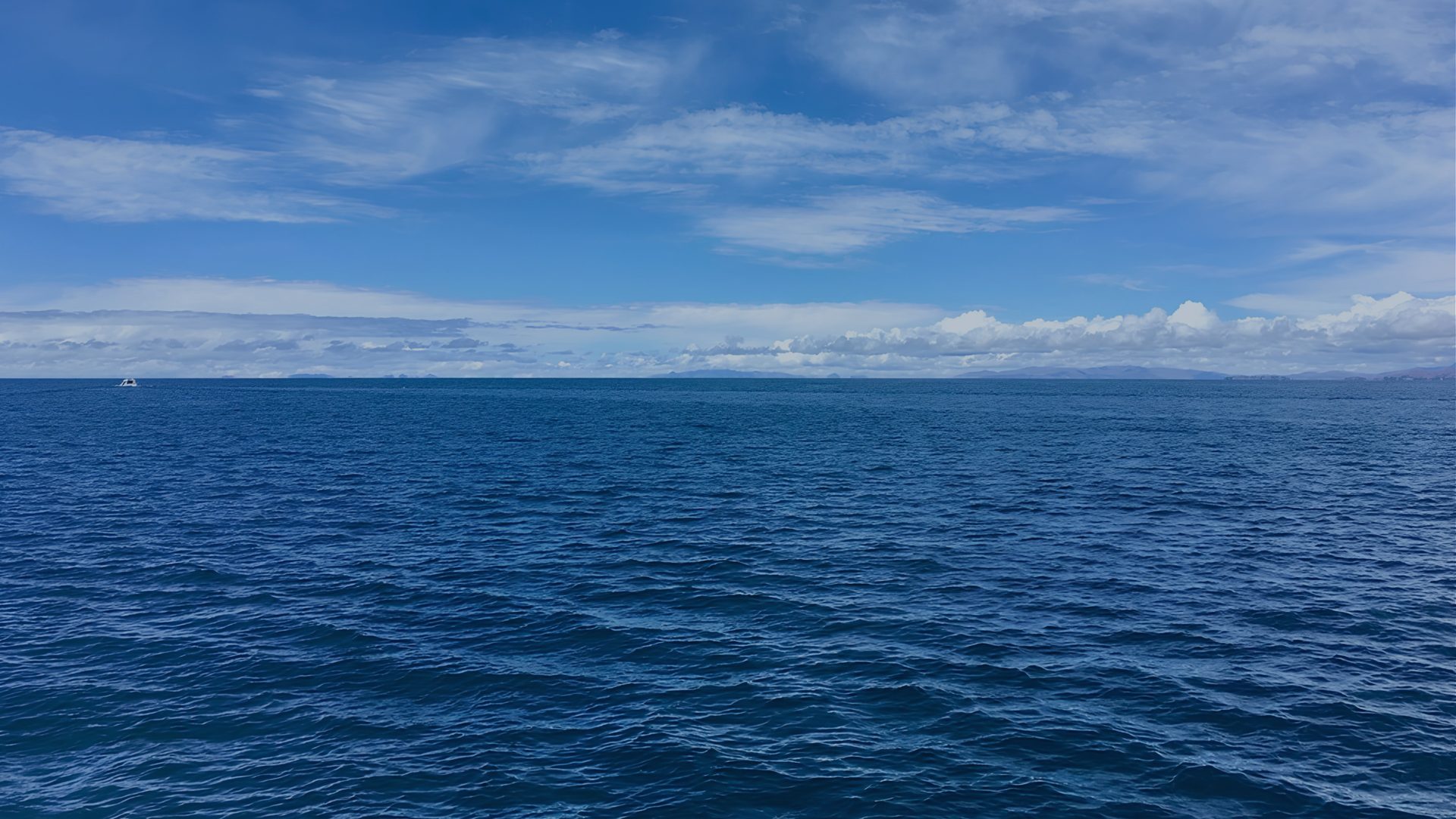 A calm sea meets a hazy horizon under a sky scattered with light cloud.