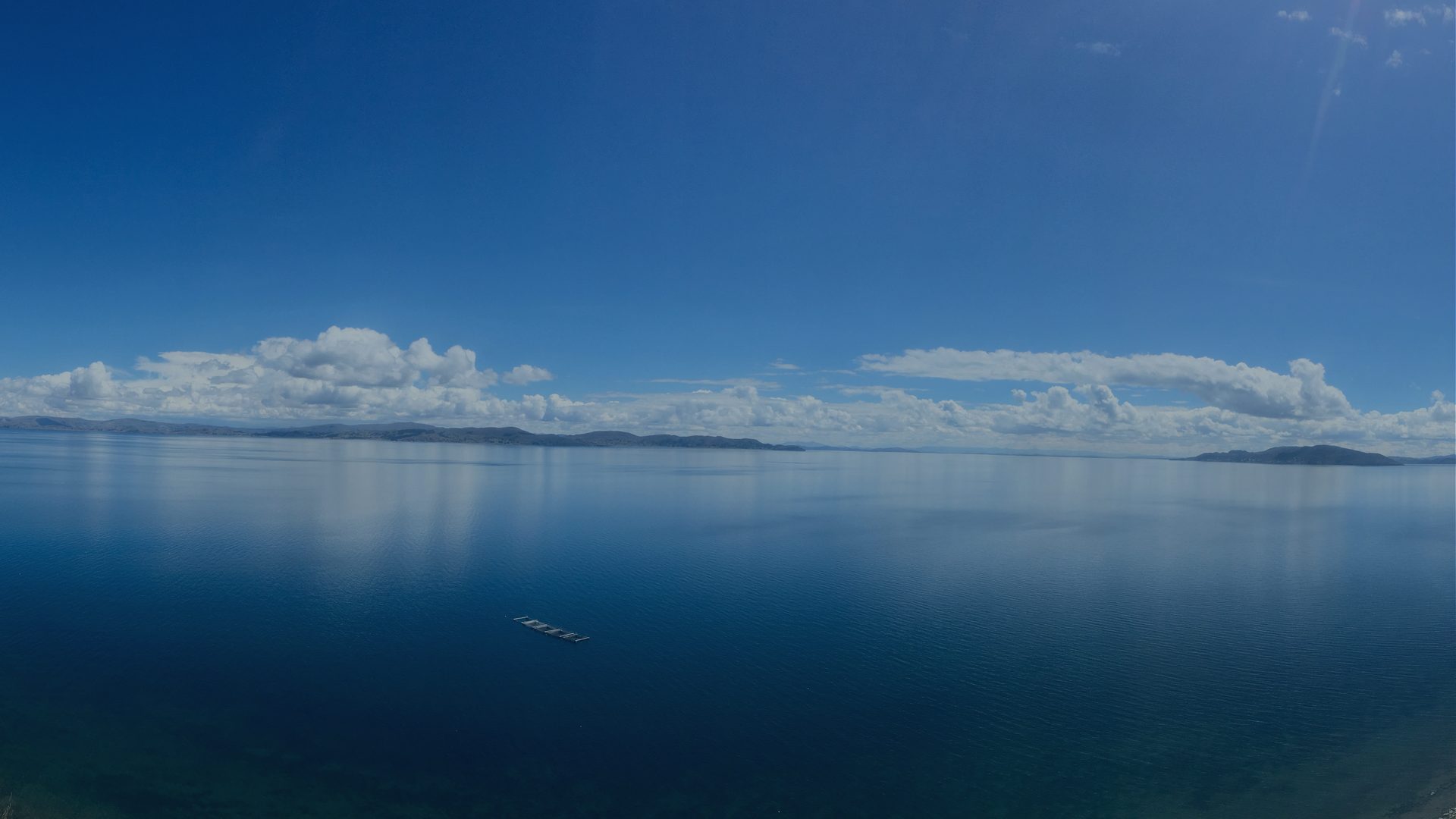A calm lake stretches to a hazy horizon under a wide, clear sky.